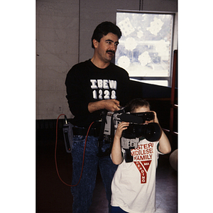 Child holding television camera with help from IBEW camera operator