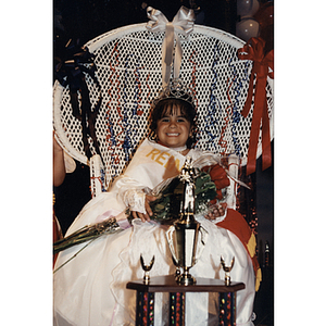 La Reina Infantil sits in a chair holding roses at the Festival Puertorriqueño