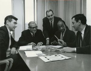 Five male members of business administration sitting and standing around a table