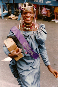 A Photograph of Marsha P. Johnson Wearing a Pearl Headpiece, Blue Dress, and a Purple “Stonewall” Sash
