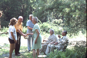Ella and Arthur Rosenburg (seated on right) greeting friends at Moon Barn Raising at entrance to Hopkins Forest on 2 August 1975. Steven Masters in straw hat at left and Harvey Cummings shakes hand of Martha Ferris in center.