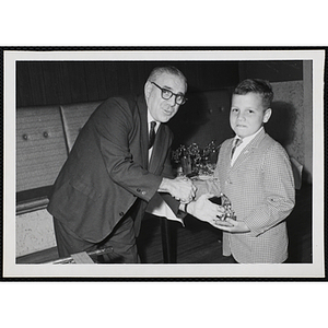 A Dad's Club member hands out a bowling league trophy to a boy