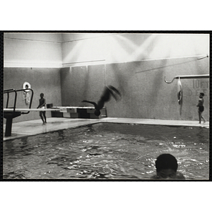 A boy performs a back flip off a diving board in a natorium pool