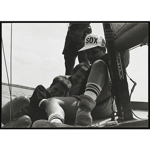 A Group of boys sitting next to the mast on a sailboat