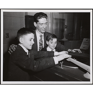 A man poses with two boys at a turntable in a radio studio