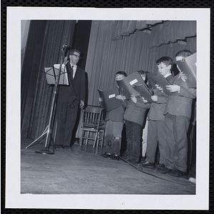 A man conducts a boys' choir on stage during a Christmas party