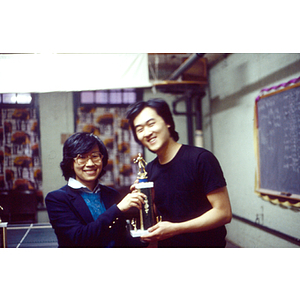 Champion of the table tennis competition stands holding his trophy with Suzanne Lee