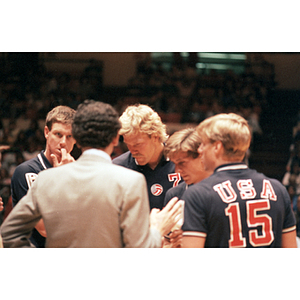 Members of the United States Men's Volleyball Team stand in a huddle with their coach