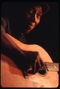 Mississippi John Hurt: studio portrait, seated, playing guitar