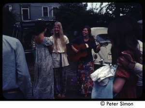 Woman with a guitar and friends gathering near parked cars, Tree Frog Farm Commune