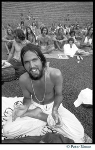 Audience member seated on the lawn, clapping, as he awaits the appearance of Ram Dass at Andrews Amphitheater, University of Hawaii