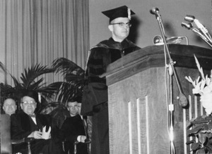 John W. Lederle dressed in academic regalia, standing at a podium