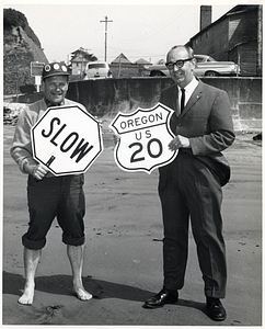 Two unidentified men posing with road signs on a beach