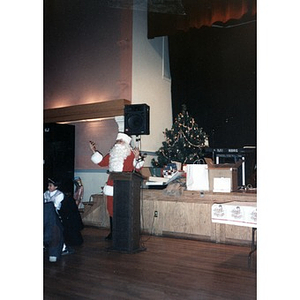 Santa Claus at the podium at the Jorge Hernandez Cultural Center during a community celebration.
