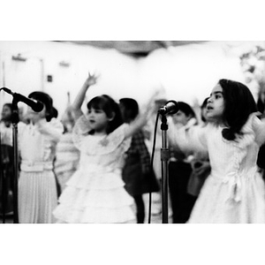 Little girls dressed up in their best raise their hands and sing into microphones placed before them.