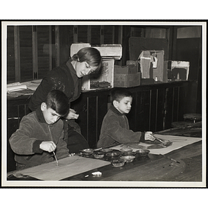 Two boys working on their paintings as an instructor looks on at the South Boston Boys' Club