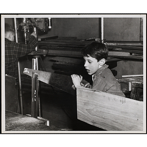 A boy from the Boys' Clubs of Boston using a crosscut saw for his woodworking project
