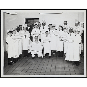 Members of the Tom Pappas Chefs' Club, Chefs' Club Committee member Mary A. Sciacca and unidentified kitchen staff pose for a group portrait with decorated cakes in a Brandeis University kitchen