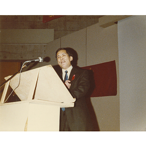 Man speaks at the podium at the 30th anniversary celebration of the People's Republic of China held in the Josiah Quincy School auditorium