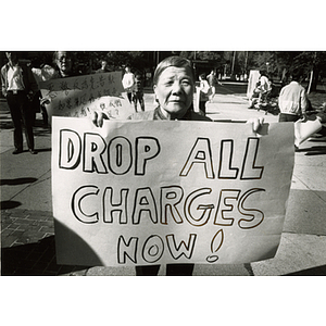 Elderly Chinese woman holds a sign that reads, "Drop All Charges Now!" at a protest for Long Guang Huang