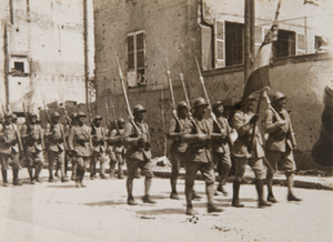 View of soldiers with bayonets marching along a town street