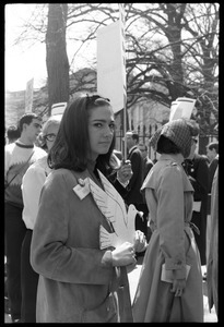 Woman holding a cutout cardboard peace dove and antiwar demonstrators standing in front of the White House during the March on Washington