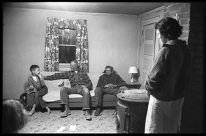 Richard Loving (center) seated on a couch, flanked by his son Donald (?) and father, Mildred Loving standing by the wall