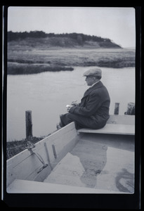 Unidentified man seated on a the edge of rowboat, looking over a pond