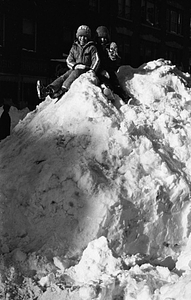 Unidentified children sitting on large snow pile