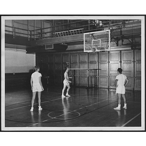 Three men in white uniforms standing on basketball court watching point being scored