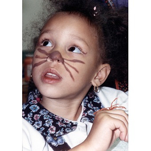 Little girl with an animal nose and whiskers painted on her face.