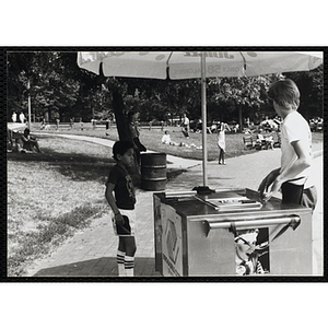 A teenage boy operates an ice juice food cart on Boston Common as boy looks on