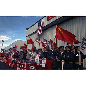 People stand in a line holding flags and posters for an event at Boston Logan Airport to welcome Zhu Rongji, Premier of the People's Republic of China