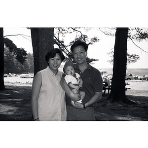 Man and woman pose with an infant in an wooded picnic area