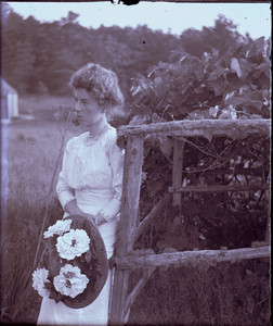 Woman with flowered hat leaning against a fence, Mashpee, Mass.