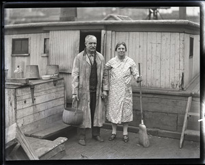 Capt. Fred Hutchins of Bucksport, Me., who was tied up with his wife in houseboat at South Station: Fred and Dellie Hutchins, standing on the boat with kettle and broom