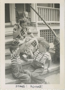 Bernice Kahn with sons Joel and Paul holding a small snake on front stairs of house