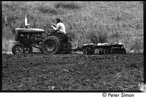 Harvey Wasserman driving a tractor with disc tiller, Montague Farm Commune