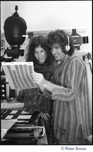 Usha (Cathy Brown) and Peter Simon in a darkroom, next to an enlarger, examining a sheet of negatives