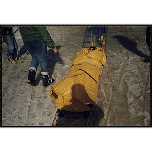 A boy strapped to a ski gurney sled is pulled over snow