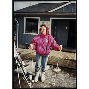 A girl in ski boots holds ski poles at resort