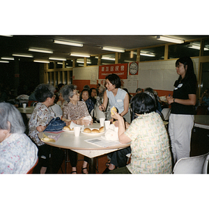 Woman offers a microphone to a table of women to speak at a Chinese Resident Association meeting