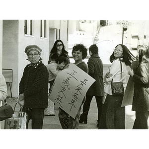 Eight women stand at the corner of Powell Street with protest signs