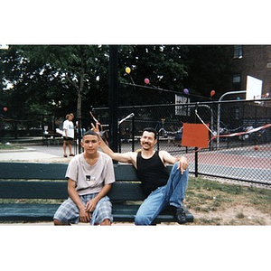 Two men sitting on a park bench in the playground during some special community event.