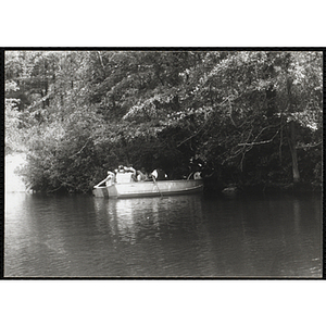 Five youth and a supervisor sit in a rowboat near trees