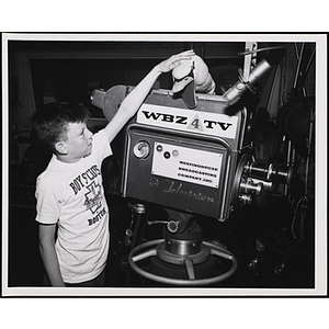 A boy pets a puppet on top of a camera in a WBZ TV studio