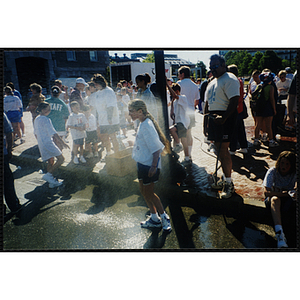 A man cools a girl with water from a hose at the Battle of Bunker Hill Road Race