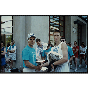 A man presents another man with a certificate as he shakes his hand at the Battle of Bunker Hill Road Race