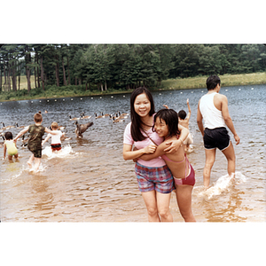 Girls hug each other while standing in the shallows of a lake