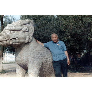 Association member poses with a dragon statue in an outdoor park